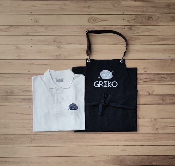 White polo t-shirt with small grey logo and black bib apron with leather straps and grey print, custom made by RestroCart, New Delhi