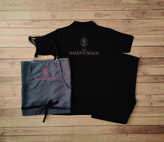 Black polo t-shirt with pink embroidered logo and grey bib apron with black ties and matching logo, custom made by RestroCart, New Delhi