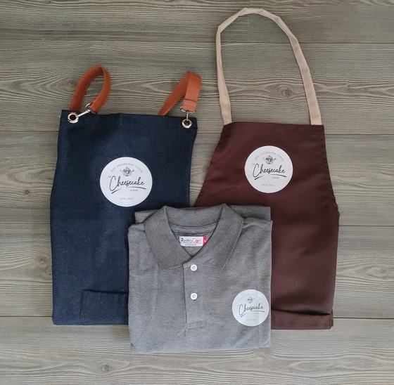Denim and brown bib aprons with round white logo patch and a grey polo t-shirt with matching logo, custom made by RestroCart, New Delhi