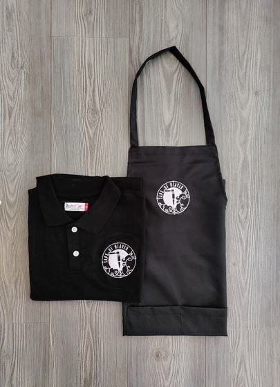 Black polo t-shirt and dark grey bib apron, both with round white printed logo, custom made by RestroCart, New Delhi