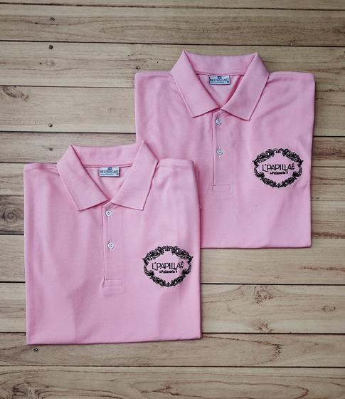 Pair of folded pink polo t-shirts with black printed ornate wordmark logo on the chest, on wood, custom made by RestroCart, New Delhi