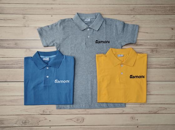Grey, blue and yellow polo t-shirts with black printed wordmark on the chest, laid flat on wood, custom made by RestroCart, New Delhi