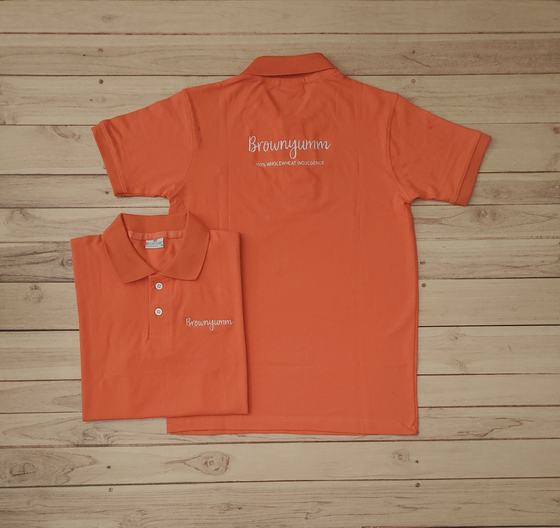 Orange polo t-shirts with white printed script wordmark on the chest, one folded and one laid flat, custom made by RestroCart, New Delhi