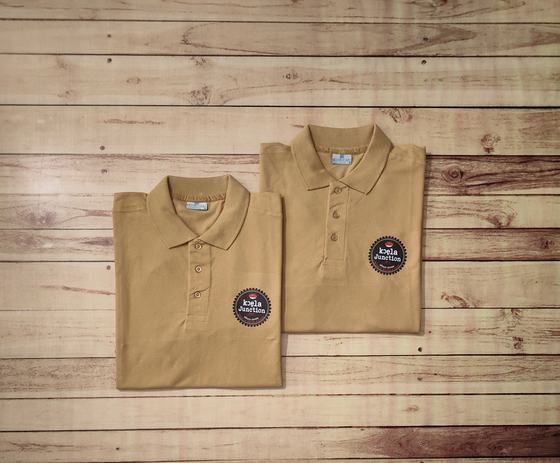 Pair of folded beige polo t-shirts with round black and white printed logo patch on the chest, custom made by RestroCart, New Delhi