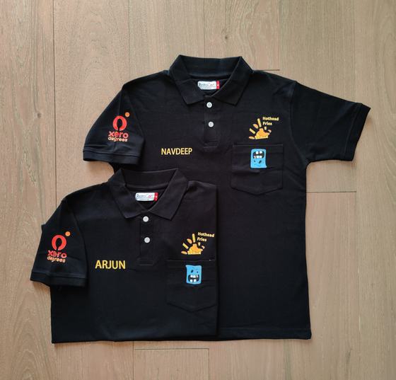 Black polo t-shirts with sleeve logo, embroidered staff names and pocket mascot patches, custom made by RestroCart, New Delhi