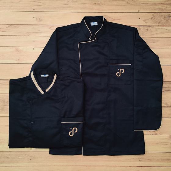 Two navy chef coats with beige collar and piping and gold embroidered monogram logo, laid flat, custom made for Pour & Palate by RestroCart, New Delhi