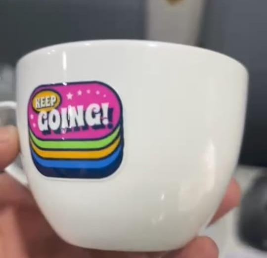 White ceramic cup with colourful printed Keep Going sticker style graphic, held in hand, custom made by RestroCart, New Delhi