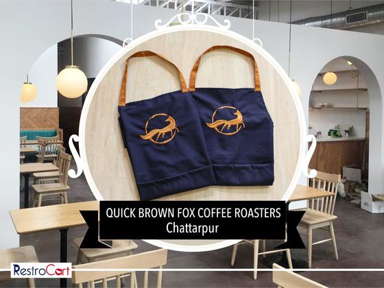 Two navy bib aprons with tan straps and large orange printed fox logo, laid flat, custom made for Quick Brown Fox by RestroCart, New Delhi