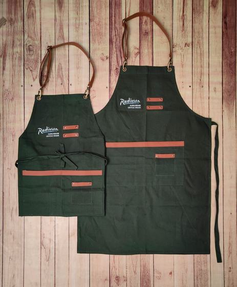 Bottle green canvas apron pair with tan leather straps, orange trims and white script logo, custom made by RestroCart, New Delhi