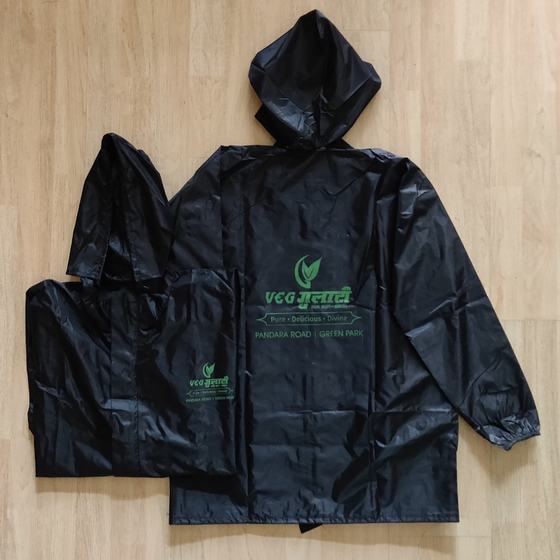 Two black hooded raincoats with green printed logo on back and chest, laid flat on light wood, custom made by RestroCart, New Delhi
