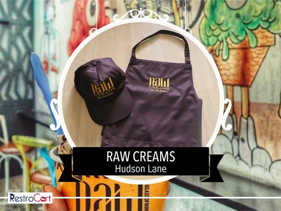 Dark brown bib apron and matching baseball cap with gold printed logo, laid flat, custom made for Raw Cream by RestroCart, New Delhi