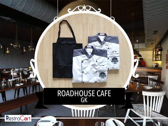 White chef coats with grey shoulder panels and round logo beside a black bib apron, custom made for Roadhouse Cafe by RestroCart, New Delhi