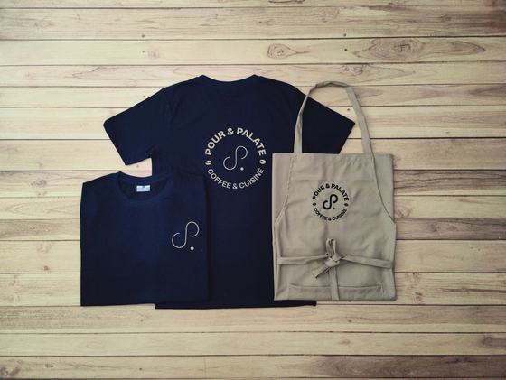 Navy round neck t-shirts with white circular logo and a beige bib apron with matching logo, laid flat, custom made by RestroCart, New Delhi