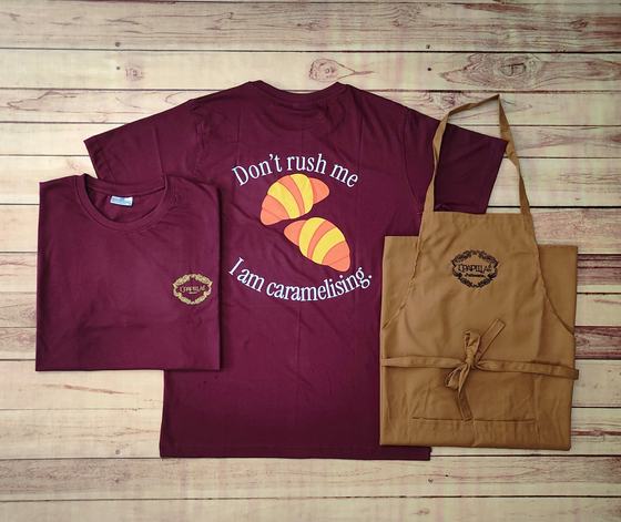 Maroon round-neck t-shirts with croissant slogan print on the back and tan bib apron with logo, custom made by RestroCart, New Delhi