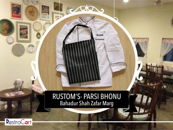 White chef coat with black piping and a black and white striped bib apron, laid flat, custom made for Rustoms by RestroCart, New Delhi