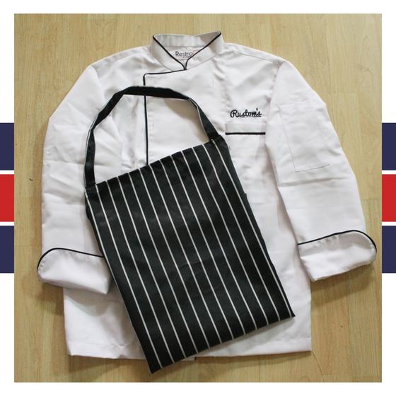White chef coat with black piping and script logo, with black and white pinstripe bib apron, custom made for Rustoms by RestroCart, New Delhi