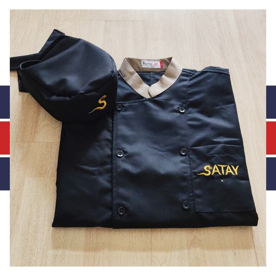 Black chef coat with beige collar and gold embroidered logo, with matching black skull cap, folded, custom made for Satay by RestroCart, New Delhi