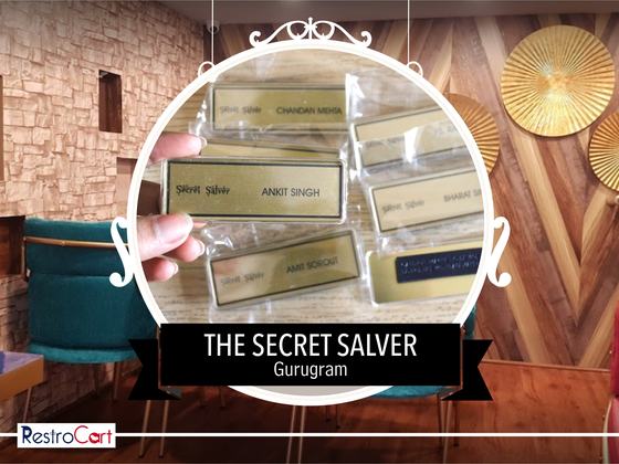 Gold rectangular name badges with printed logo and staff names in clear sleeves, one held, custom made for Secret Salver by RestroCart, New Delhi