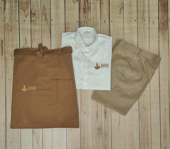 White service shirt, beige trousers and brown waist apron with pocket, all with embroidered cup logo, custom made by RestroCart, New Delhi