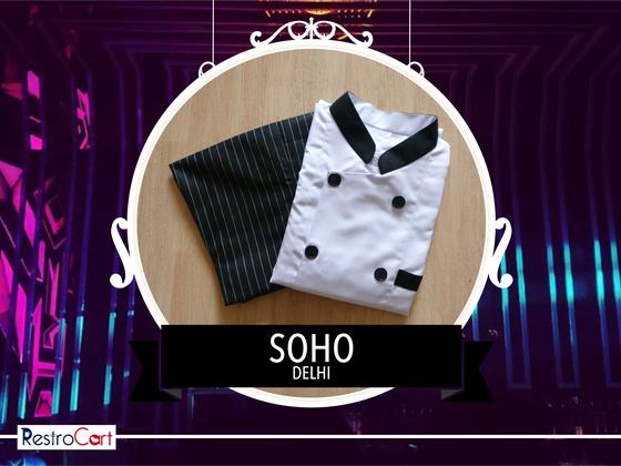 White double-breasted chef coat with black collar beside a black pinstripe apron, custom made for Soho by RestroCart, New Delhi