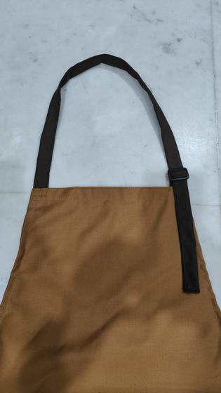 Plain golden brown canvas bib apron with dark brown adjustable neck strap, hanging, custom made by RestroCart, New Delhi