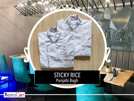 White long-sleeve chef coats with black piping and gold logo, one folded over another, custom made for Sticky Rice by RestroCart, New Delhi