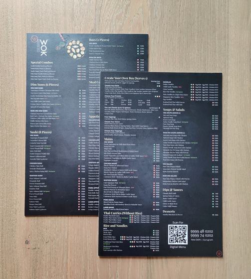 Two dark sunboard menu sheets with printed dish lists, photos and QR code, on light wood, custom made by RestroCart, New Delhi