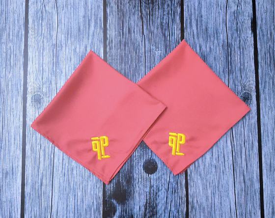 Coral pink cloth table napkins with bold yellow embroidered logo, laid at an angle, custom made by RestroCart, New Delhi