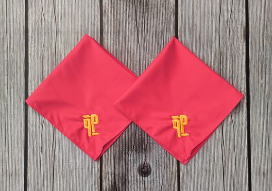 Pair of red cloth table napkins folded into diamonds with yellow embroidered monogram, on grey wood, custom made by RestroCart, New Delhi
