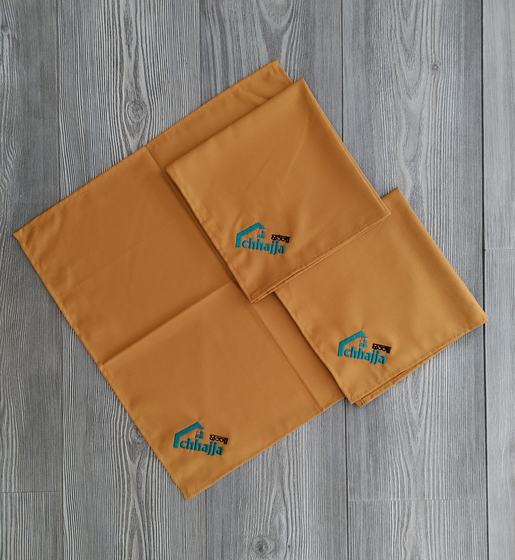 Mustard yellow table napkins with teal printed logo in the corner, folded on grey wood, custom made by RestroCart, New Delhi