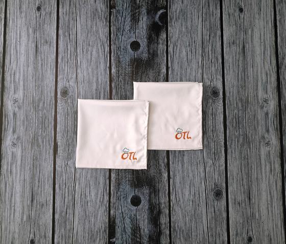 White cloth table napkins with orange and grey embroidered corner logo, laid overlapping, custom made by RestroCart, New Delhi