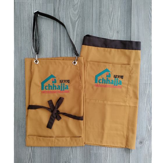 Mustard bib and waist aprons with brown trim and ties, printed teal logo, laid flat on grey wood, custom made for Tapri by RestroCart, New Delhi