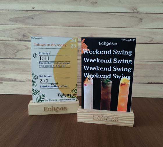 Two printed promo tent cards held in engraved pine wood block stands on a wooden table, custom made by RestroCart, New Delhi