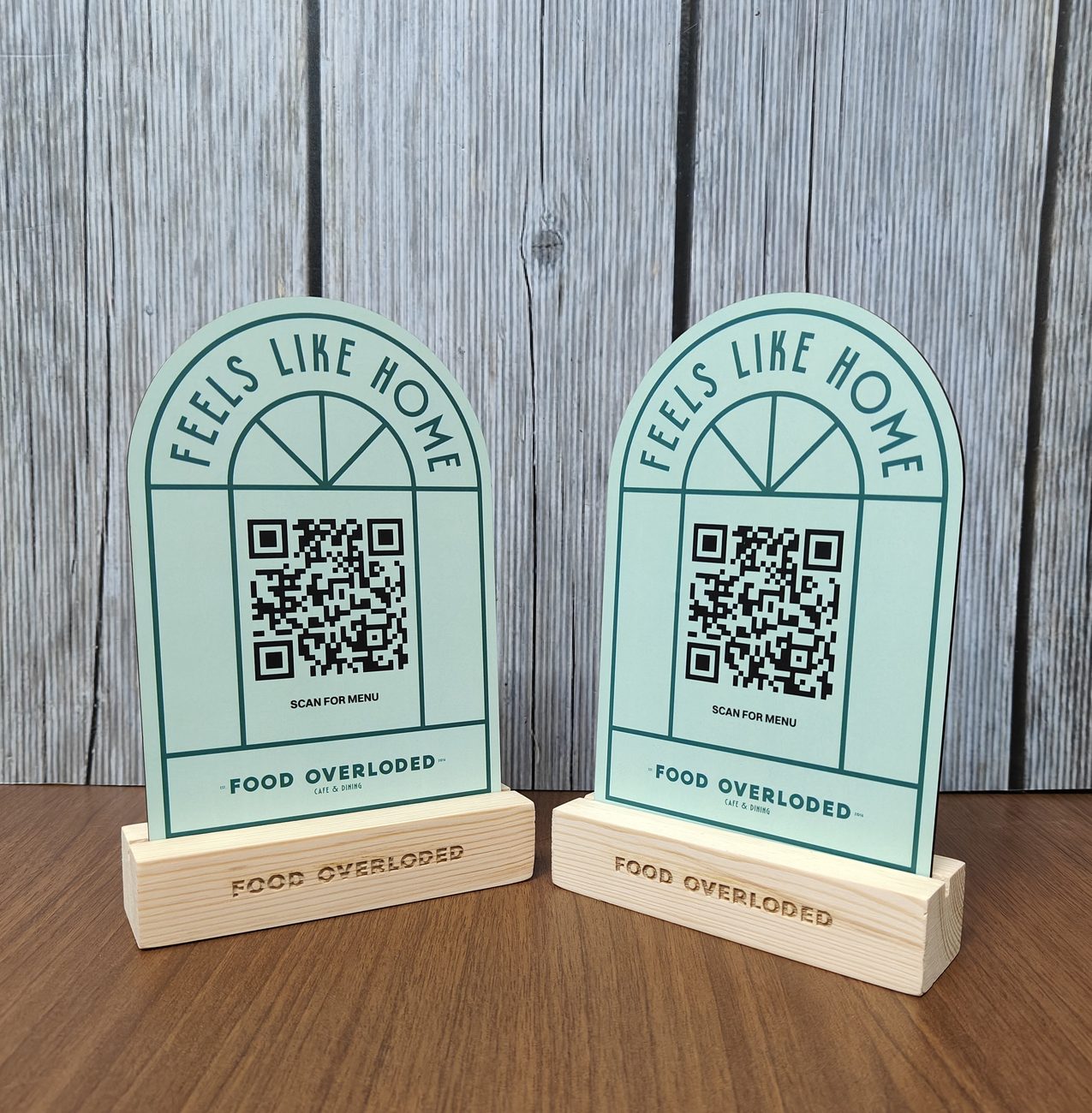 Arch-shaped QR code table stands on engraved wooden bases printed 'Feels like home' for Food Overloaded, made by RestroCart