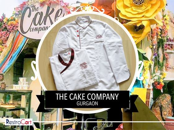 White chef coats with red piping and maroon collar trim and small logo, one folded, custom made for The Cake Company by RestroCart, New Delhi
