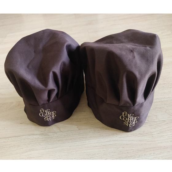 Two brown pleated chef hats with gold embroidered script logo on band, close-up, custom made for The Coffee Shop by RestroCart, New Delhi