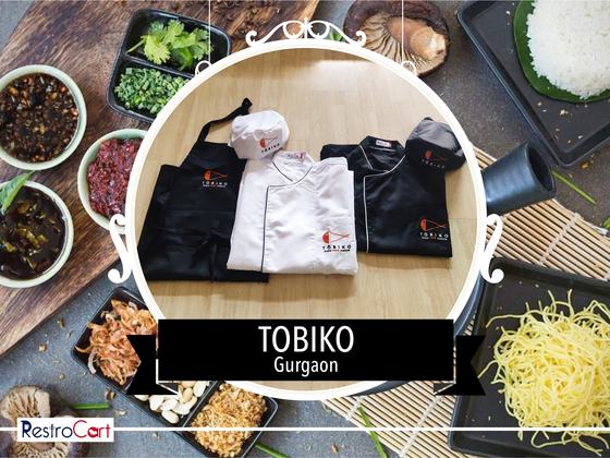 Black bib apron, white and black chef coats with orange logo and matching chef caps, custom made for Tobiko by RestroCart, New Delhi