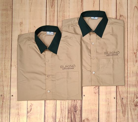 Beige uniform shirts with contrast dark green collar and tonal embroidered pocket logo, custom made by RestroCart, New Delhi