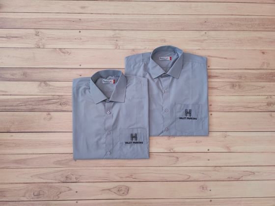 Two grey valet shirts with black printed logo on the pocket, folded and overlapping on wood, custom made by RestroCart, New Delhi