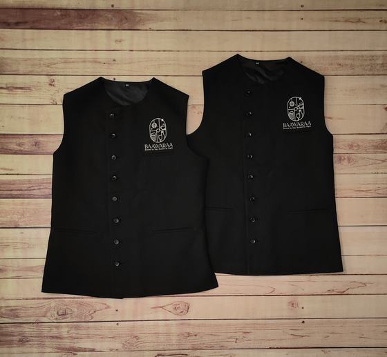 Pair of black round neck waistcoats with grey embroidered crest logo and button front, laid flat, custom made by RestroCart, New Delhi