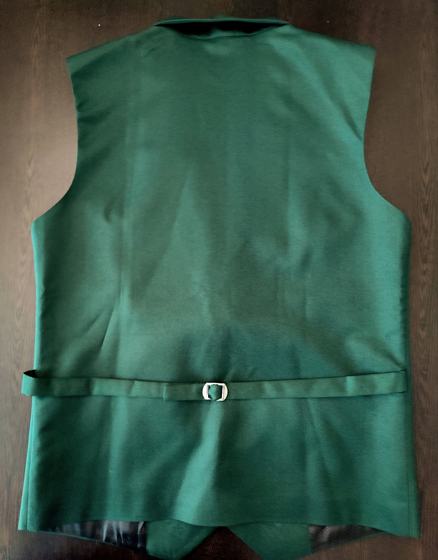 Back view of a green waistcoat with adjustable half belt and dark lining, on a dark surface, custom made by RestroCart, New Delhi