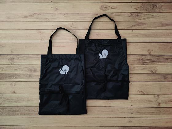 Pair of black waterproof bib aprons with white printed squirrel logo and waist ties, laid flat, custom made by RestroCart, New Delhi