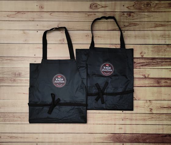 Pair of black waterproof bib aprons with round red and white printed logo, laid flat on wood, custom made by RestroCart, New Delhi