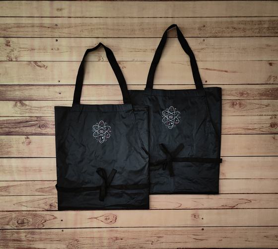 Pair of black waterproof bib aprons with white printed emblem logo and black waist ties, laid flat, custom made by RestroCart, New Delhi
