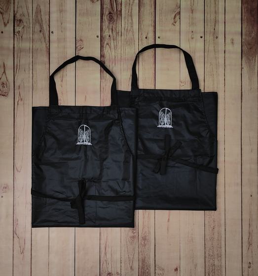 Two black waterproof bib aprons with white printed arch logo and black neck and waist straps, custom made by RestroCart, New Delhi