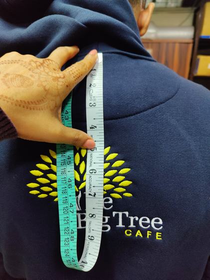 Close-up of navy hoodie back with embroidered tree logo being measured with a green tape measure, custom made by RestroCart, New Delhi