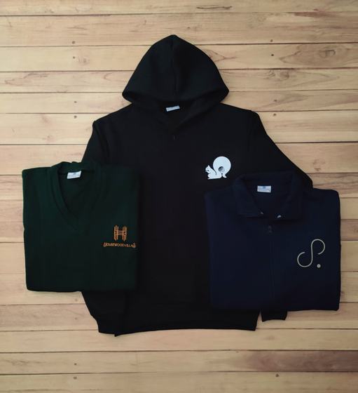 Black hoodie with white squirrel logo, green V-neck sweater and navy zip jacket with logo, laid flat, custom made by RestroCart, New Delhi