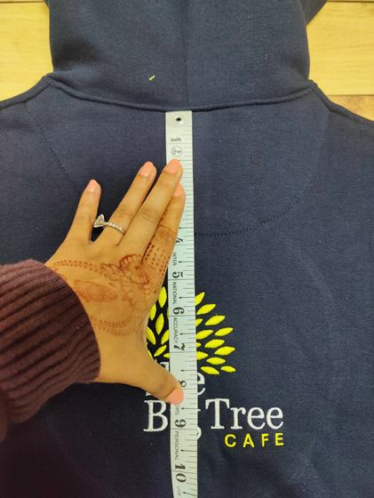 Close-up of navy hoodie back with yellow and white embroidered tree logo being measured with a ruler, custom made by RestroCart, New Delhi