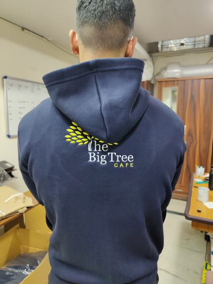 Back view of navy hoodie with yellow and white embroidered tree logo, worn by a man in a workshop, custom made by RestroCart, New Delhi