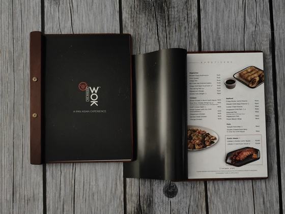 Wooden spine menu with black cover and screw posts, open to a printed page with dish photos, custom made by RestroCart, New Delhi
